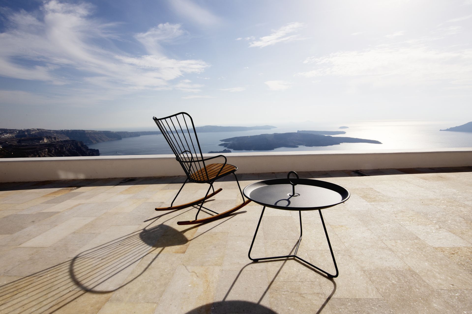 Der Houe Eyelet Beistelltisch von HOUE und der Houe Click Rocking Chair auf einer Terrasse mit Blick auf das Meer.