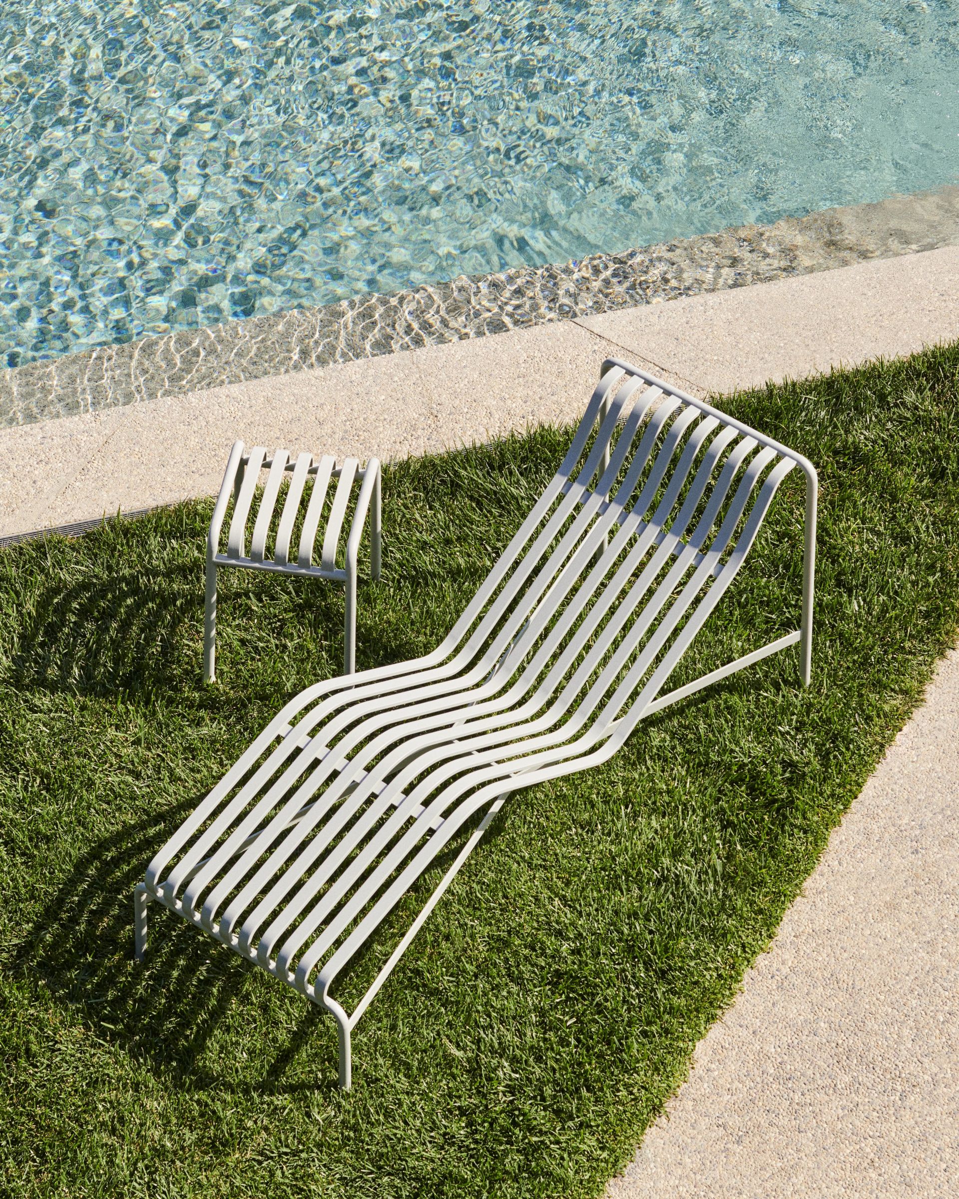Die HAY Palissade Chaise Lounge auf einen Stück Rasen vor einem Pool. 