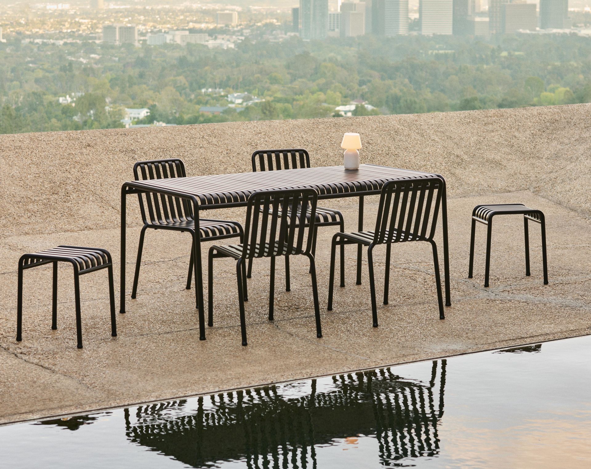 Der HAY Palissade Tisch in anthrazit mit mehreren Palissade Dining Stühlen auf einer Terrasse mit toller Aussicht. 